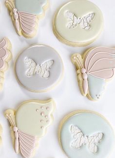 decorated cookies are arranged in pastel colors on a white tablecloth with butterfly decorations