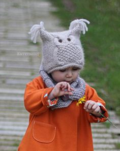 a small child wearing an orange coat and a gray knitted hat holding a flower