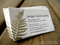 a business card sitting on top of a wooden table with a fern leaf logo printed on it