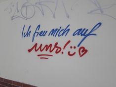 graffiti written on the side of a white wall with red and blue writing underneath it