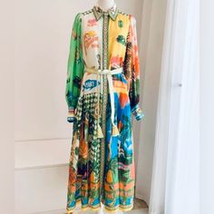 Step Into A Vibrant World Of Color With This Shirtdress In The Paradise Inn Print. Made From Lightweight Polyester, This Maxi Dress Boasts A Dropped Waist, Gathered Skirt, And Balloon Sleeves. The Woven Jacquard Tie Belt With Tassel Ends Adds An Elegant Touch. With A Flowing Skirt That Moves Beautifully, This Dress Is Ideal For Those Special Moments In Life. Silk Dress With Vibrant Green Print, Silk Dresses With Vibrant Green Print, Vibrant Green Silk Dress With Print, Green Silk Dress With Vibrant Print, Yellow Printed Long Sleeve Midi Dress, Long Sleeve Printed Yellow Midi Dress, Green Long Sleeve Maxi Dress With Vibrant Print, Yellow Silk Long Sleeve Dress, Yellow Long Sleeve Midi Dress For Vacation