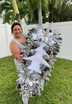 a woman is holding a christmas wreath in the grass with pine cones and snowflakes on it