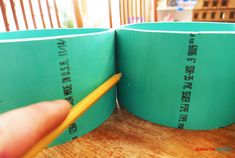 a person holding a pencil in front of two green cups