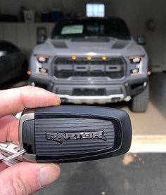 a hand holding a car key in front of a truck and another vehicle parked in the garage