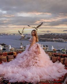 a woman in a pink dress standing on a rug with seagulls flying around her