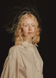 a woman with blonde hair standing in front of a black background wearing a beige shirt