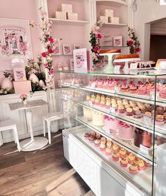 a bakery filled with lots of cupcakes on top of glass shelves next to white chairs