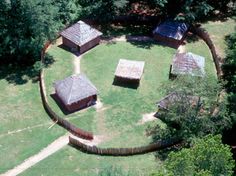 an aerial view of several small huts in the middle of a grassy area surrounded by trees