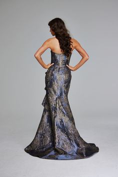 the back of a woman in a blue and gold dress with her hands on her hips