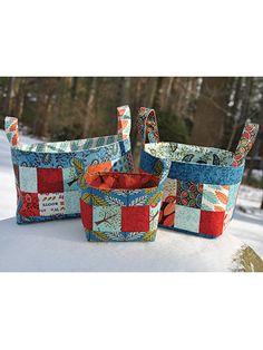 three quilted baskets sitting on top of snow covered ground with trees in the background