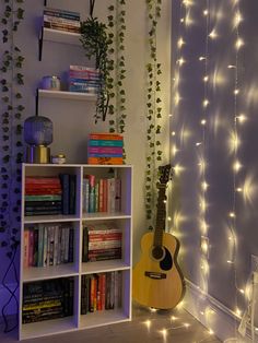 an acoustic guitar sits in front of a book shelf with books and lights on it