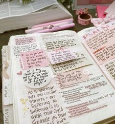 an open bible with pink and white writing on it, surrounded by other paper items