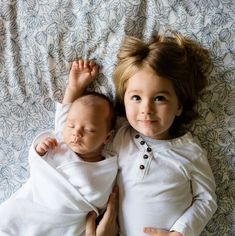 two young children laying next to each other on top of a bed with white sheets