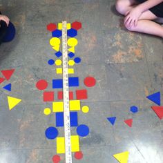 two children are sitting on the floor and one is measuring out shapes with a tape measure