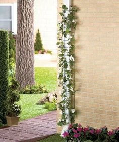 a brick wall with plants and flowers growing on it next to a sidewalk in front of a house