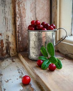 a metal bucket filled with cherries sitting on top of a wooden window sill