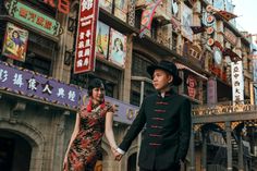 a man and woman are walking down the street in front of buildings with chinese writing on them