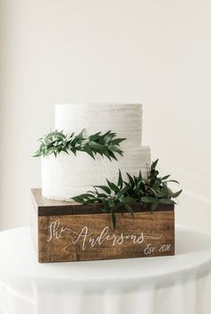 a wedding cake with greenery on top is sitting on a wooden box that says, mr and mrs