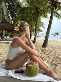 a woman sitting on top of a towel next to a coconut