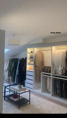 an open closet with clothes hanging on the walls and tables in front of it,