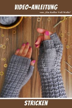 a woman's hands wearing knitted mitts and knitting needles on top of a wooden table