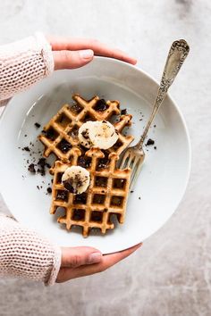 a person holding a plate with waffles and bananas on it in their hands