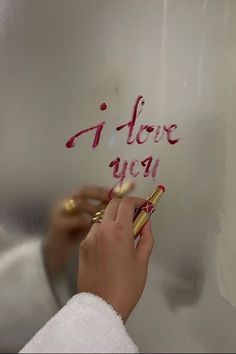 a person writing on a metal surface with pink ink and gold trimmings, while holding a pair of scissors in their left hand