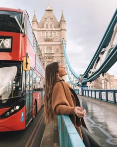 a woman standing on the side of a bridge next to a red double decker bus