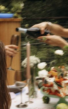 two people are pouring wine into glasses at a table with flowers and candles on it