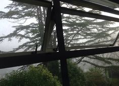 the view from inside an open window on a foggy day with trees in the background