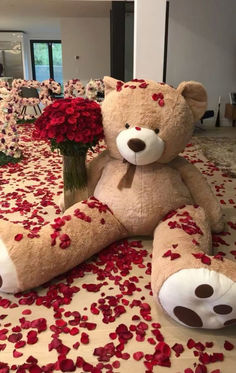 a large teddy bear sitting on top of a bed covered in red flowers and petals