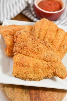 some fried food on a white plate next to a small bowl of ketchup