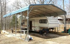 an rv parked under a metal carport in the middle of a wooded area with trees