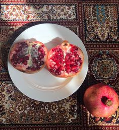 two pomegranates on a white plate next to an apple and rug