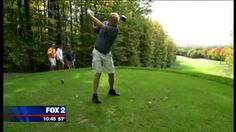 a man swinging a golf club on top of a lush green field next to trees