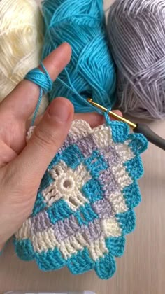 a hand holding a crochet doily next to balls of yarn