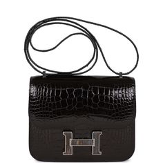 This rare Hermes Constance 18, is of Black shiny alligator with palladium and tiger's eye hardware and features tonal stitching, a "H" snap lock closure, and an adjustable shoulder strap.The interior is lined with black lambskin and has an open pocket on the front wall, a center divide, and a slit pocket on the back wall. Collection: UOrigin: FranceCondition: Pristine, new or never (Plastic on hardware)Accompanied by: Hermes box, Hermes dustbag, felt and CITESMeasurements: 7.25" width x 6.25" height x 2.25" depth; 10" double; 20" single Snap Lock, Front Wall, Hermes Constance, Hermes Box, Hermes Handbags, Tiger's Eye, New Bag, Tiger Eye, Alligator