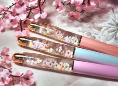 three pens sitting next to each other on top of a white table covered in pink flowers