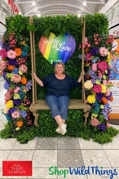 a woman sitting on a swing surrounded by flowers and greenery in a shopping mall