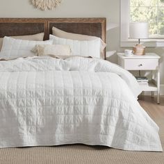 a bed with white linens and pillows in a neutral bedroom, next to a window