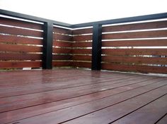 an empty wooden deck with black railings and wood slats on the top floor