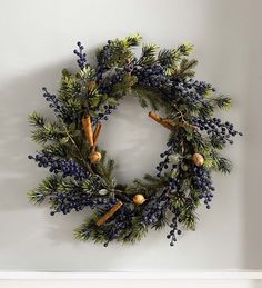 a wreath hanging on the wall with blue berries and pine cones in front of it