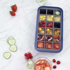 an ice tray filled with fruit and cucumbers next to sliced up strawberries