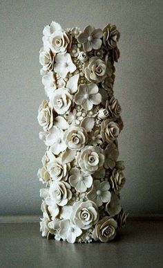 there is a tall vase made out of paper flowers on the table with white walls in the background