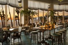 an indoor dining area with tables, chairs and umbrellas overlooking the ocean at sunset