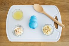 a white tray topped with two cups filled with different types of food next to a wooden spoon