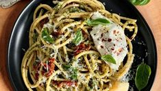 a black plate topped with pasta covered in pesto and parmesan cheese on top of a wooden table