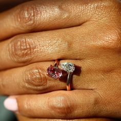 a woman's hand holding a ring with two different colored stones on it,