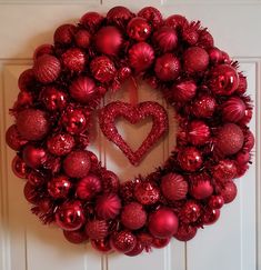 a red christmas wreath with ornaments hanging on the front door and a heart shaped ornament