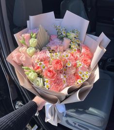 a bouquet of flowers is being held in the back of a car by someone's hand